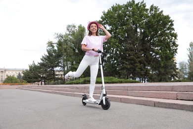 Photo of Young woman riding electric kick scooter on city street