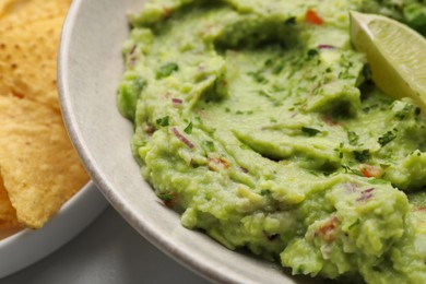 Bowl of delicious guacamole with lime and nachos chips on table, closeup