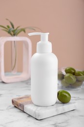 Photo of Bottle of cosmetic product with olive essential oil on white marble table