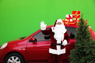 Photo of Authentic Santa Claus near car with fir tree and presents against green background