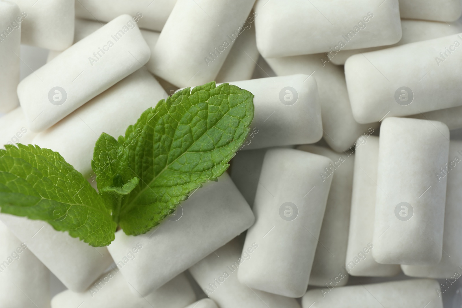 Photo of Tasty white chewing gums and mint leaves as background, top view