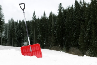 Photo of Shovel in snow near forest, space for text. Winter outdoor work