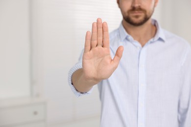 Photo of Man showing stop gesture indoors, closeup with space for text