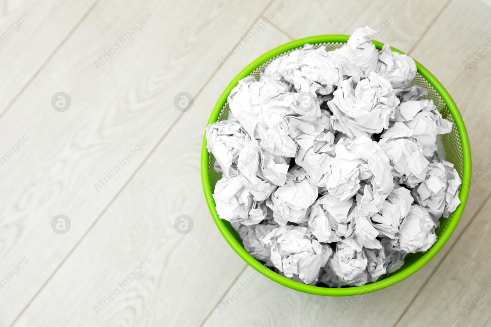 Photo of Metal bin with crumpled paper on floor, top view. Space for text