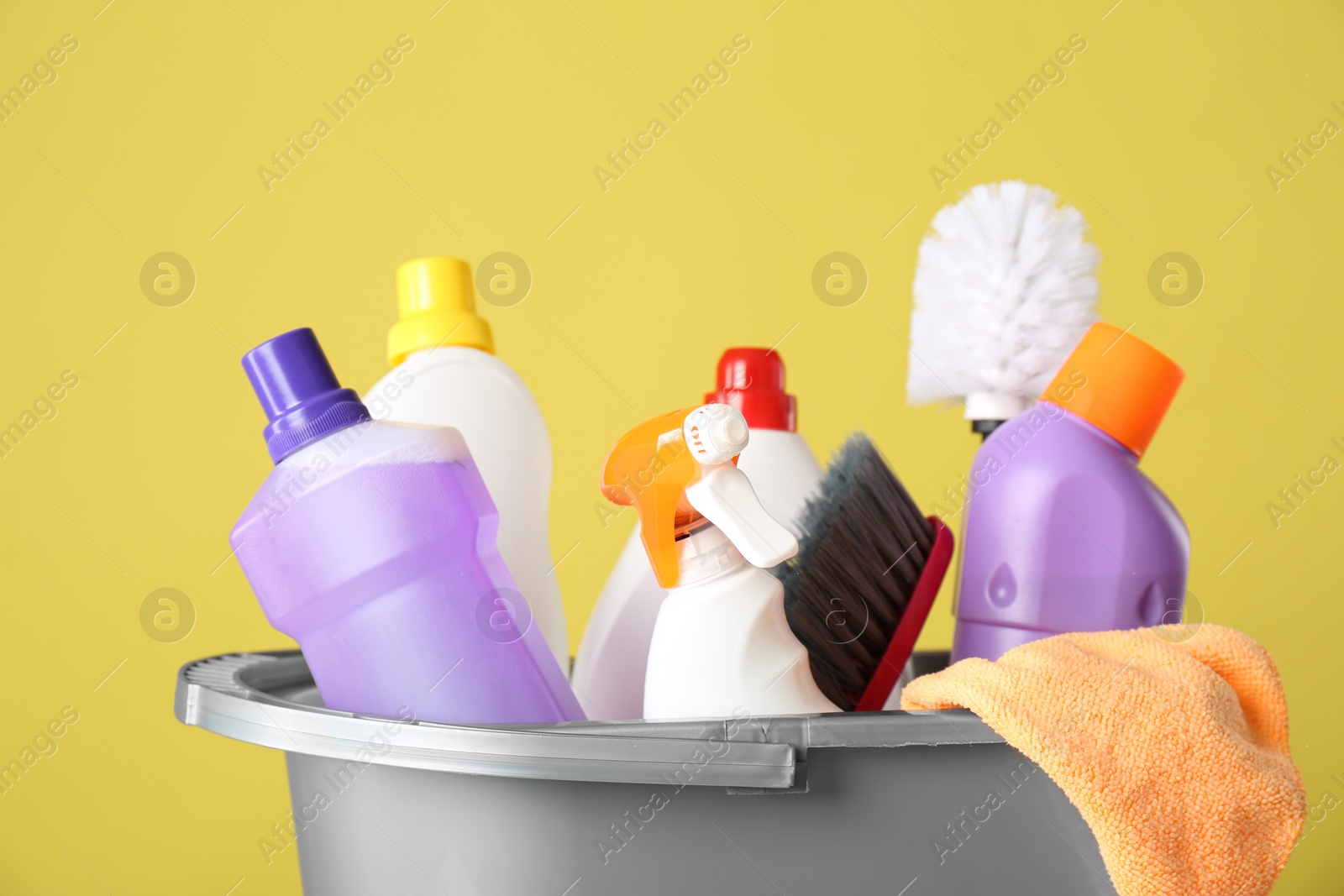 Photo of Bucket with cleaning products and tools on yellow background, closeup