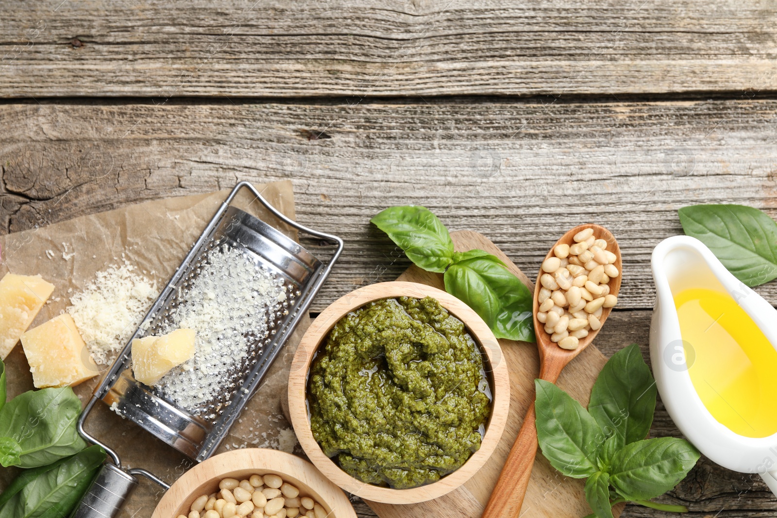 Photo of Tasty pesto sauce, basil, pine nuts, cheese, garlic and oil on wooden table, top view. Space for text