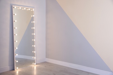 Photo of Large mirror with lamps near color wall. Space for text