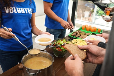 Photo of Volunteers serving food to poor people in charity centre, closeup