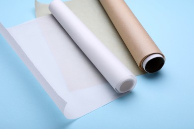 Photo of Rolls of baking paper on light blue background, closeup