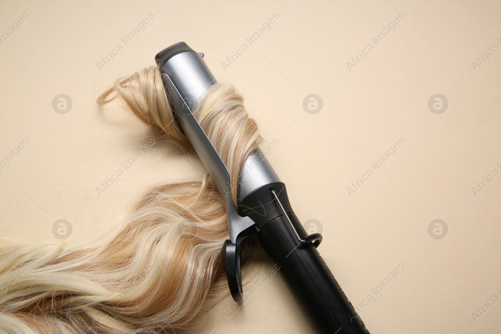 Photo of Curling iron with blonde hair lock on beige background. Space for text
