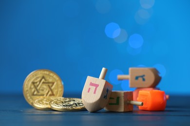 Hanukkah celebration. Dreidels with jewish letters and coins against blue background with blurred lights, closeup