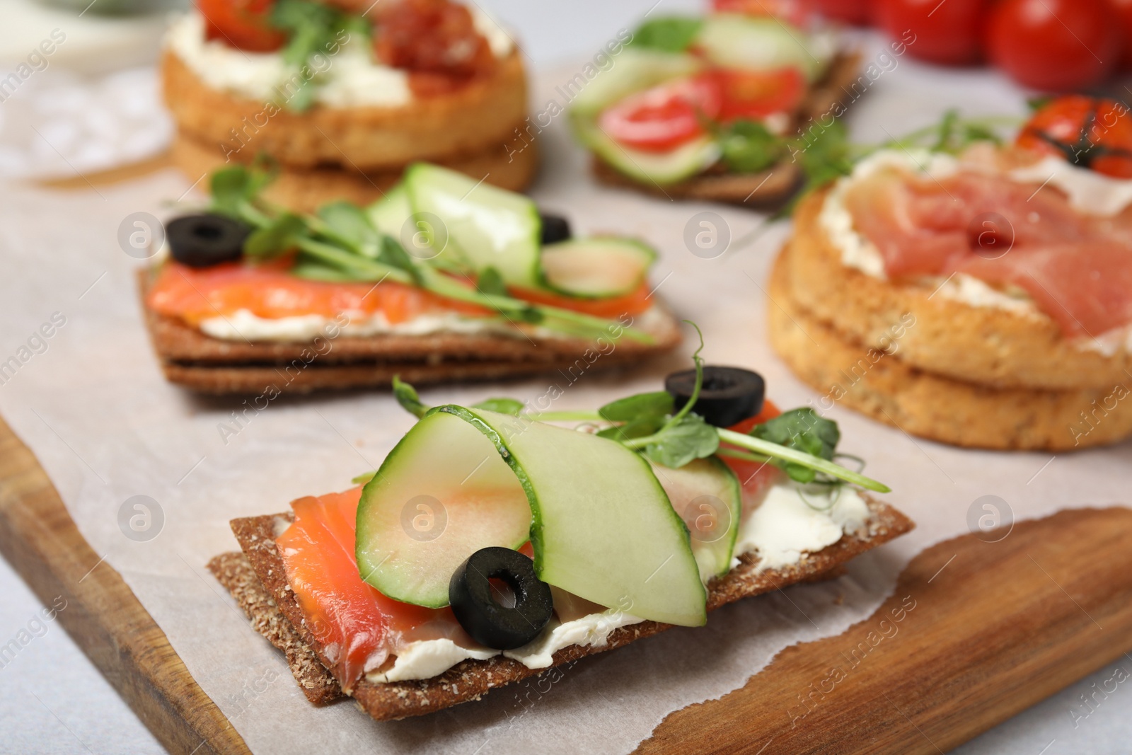 Photo of Tasty rye crispbreads with salmon, cream cheese and vegetables on wooden board. closeup