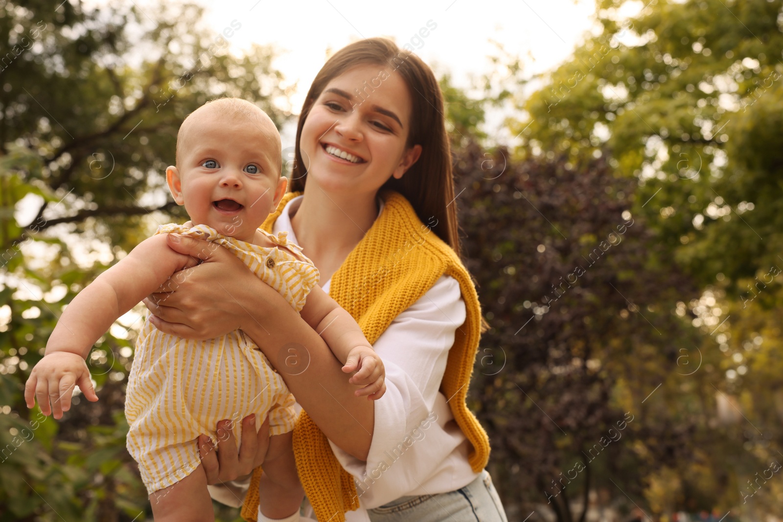 Photo of Happy mother with adorable baby walking in park on sunny day, space for text