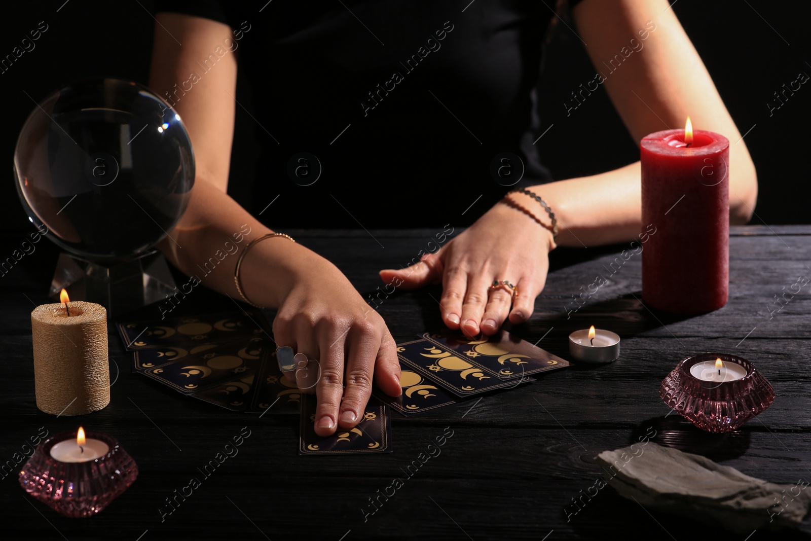 Photo of Soothsayer predicting future with tarot cards at table in darkness, closeup