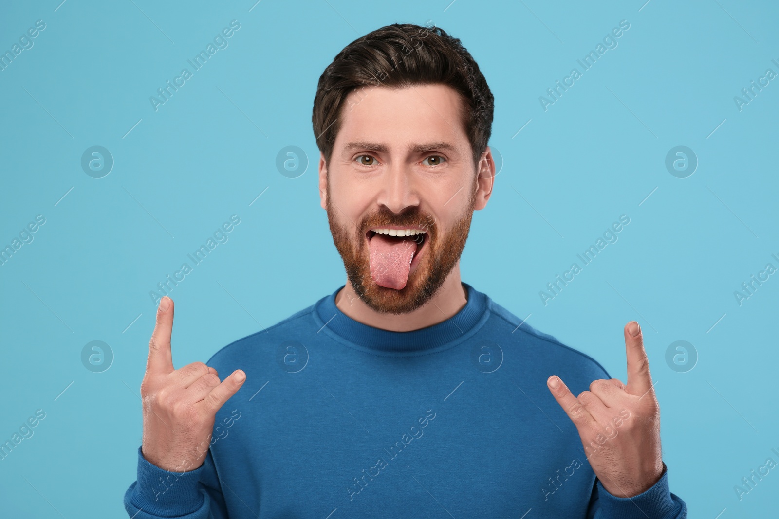 Photo of Man showing his tongue and rock gesture on light blue background