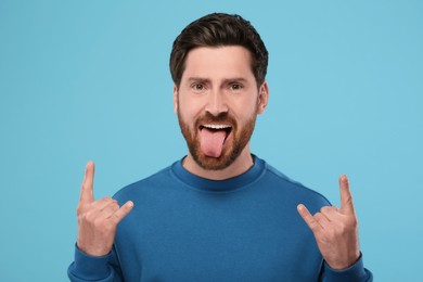 Man showing his tongue and rock gesture on light blue background