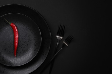 Stylish table setting. Plates, cutlery and red chilli pepper on black background, top view with space for text