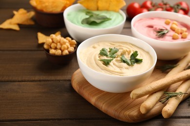 Photo of Different kinds of tasty hummus served with bread sticks on wooden table