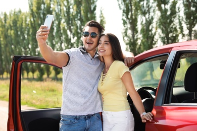 Happy young couple taking selfie near car on road