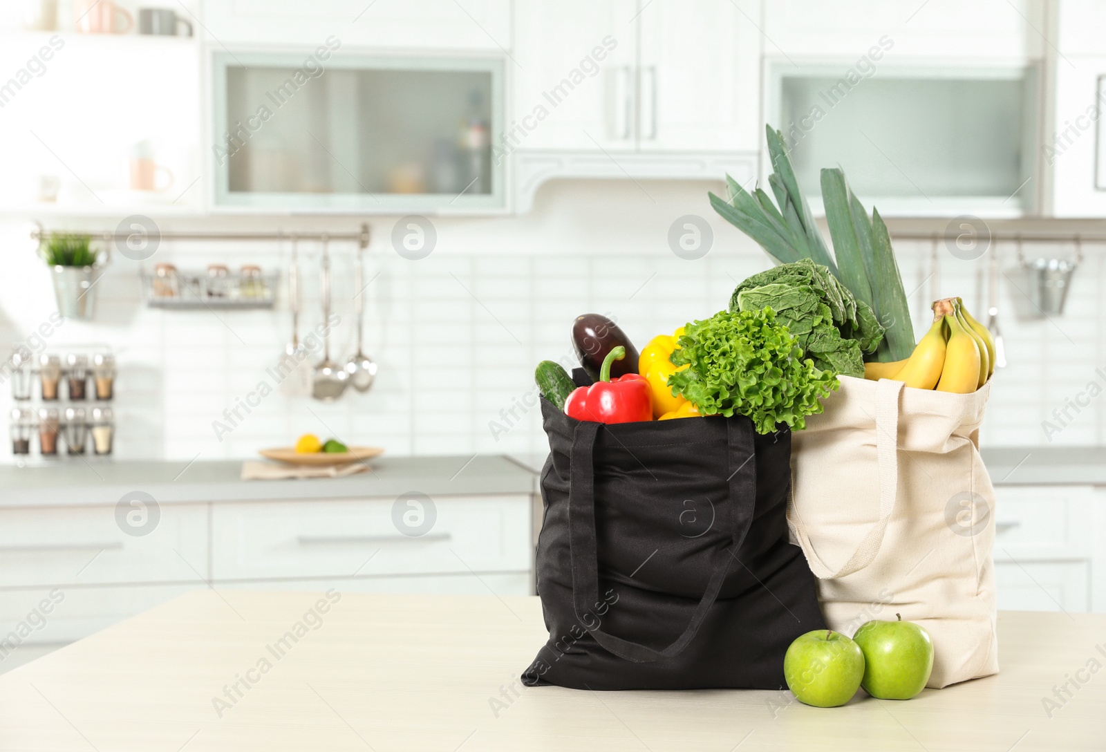 Photo of Textile shopping bags full of vegetables and fruits on table in kitchen. Space for text