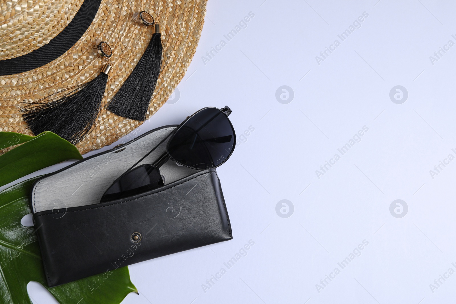 Photo of Stylish sunglasses in black leather case, straw hat and beautiful earrings on white background, flat lay. Space for text