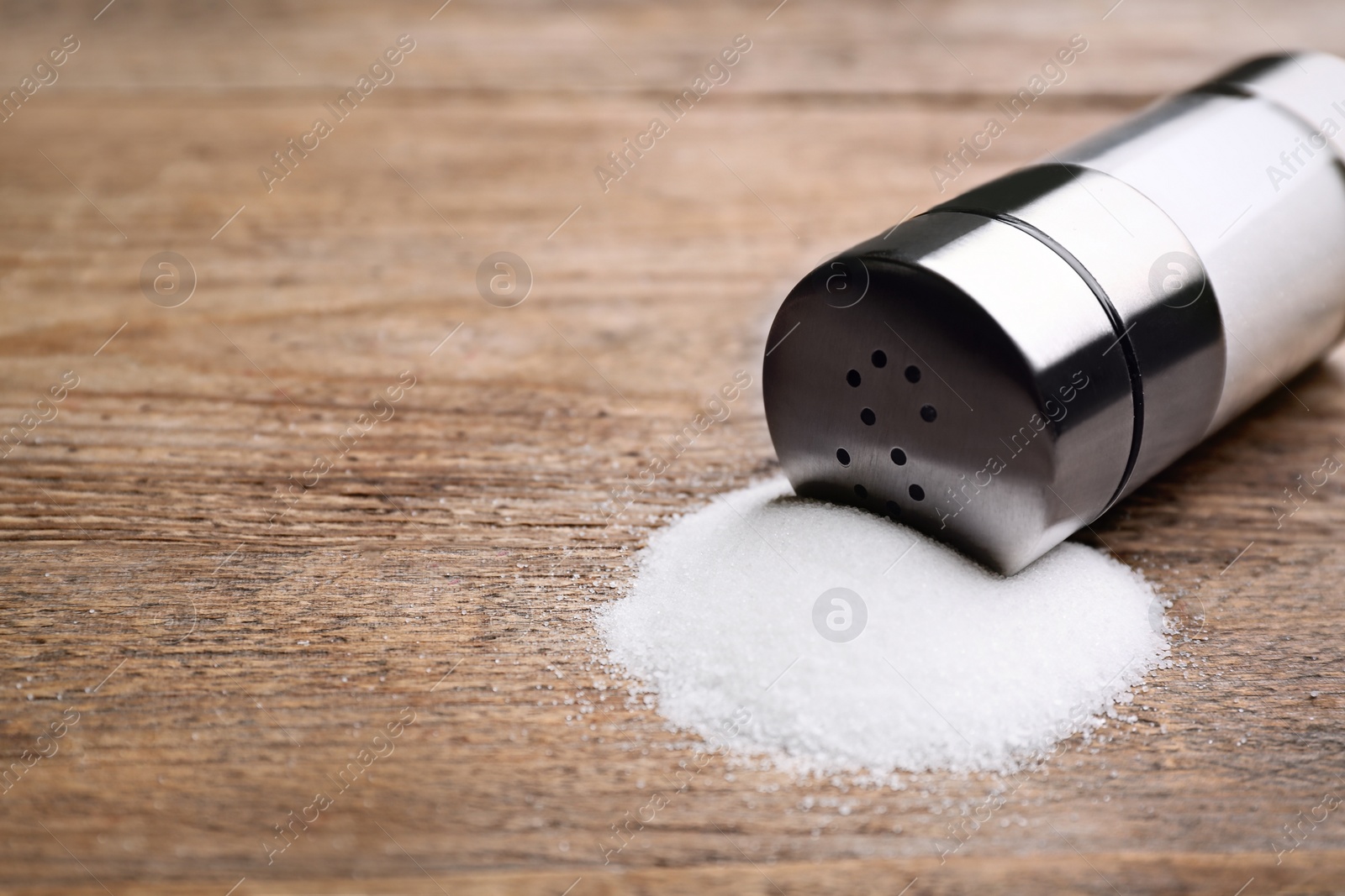 Photo of Scattered salt and shaker on wooden table, closeup. Space for text