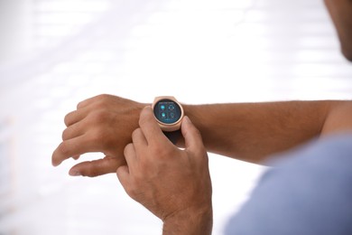 Man setting smart home control system via smartwatch against light background, closeup. App interface with icons on display