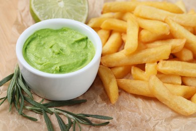 Photo of Delicious french fries, avocado dip, lime and rosemary on parchment, closeup