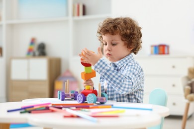 Photo of Cute little boy playing with wooden toys at white table in kindergarten