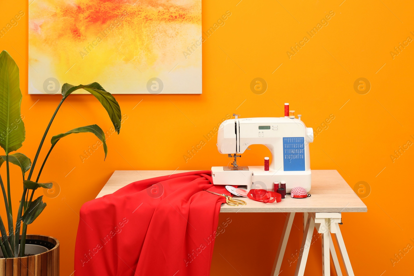 Photo of Modern sewing machine with cloth and craft accessories on wooden table near orange wall in room