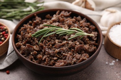 Photo of Fried ground meat in bowl and rosemary on brown textured table, closeup