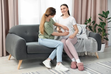 Doula taking care of pregnant woman on sofa at home. Preparation for child birth