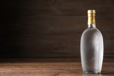 Photo of Bottle of vodka on table against wooden background. Space for text