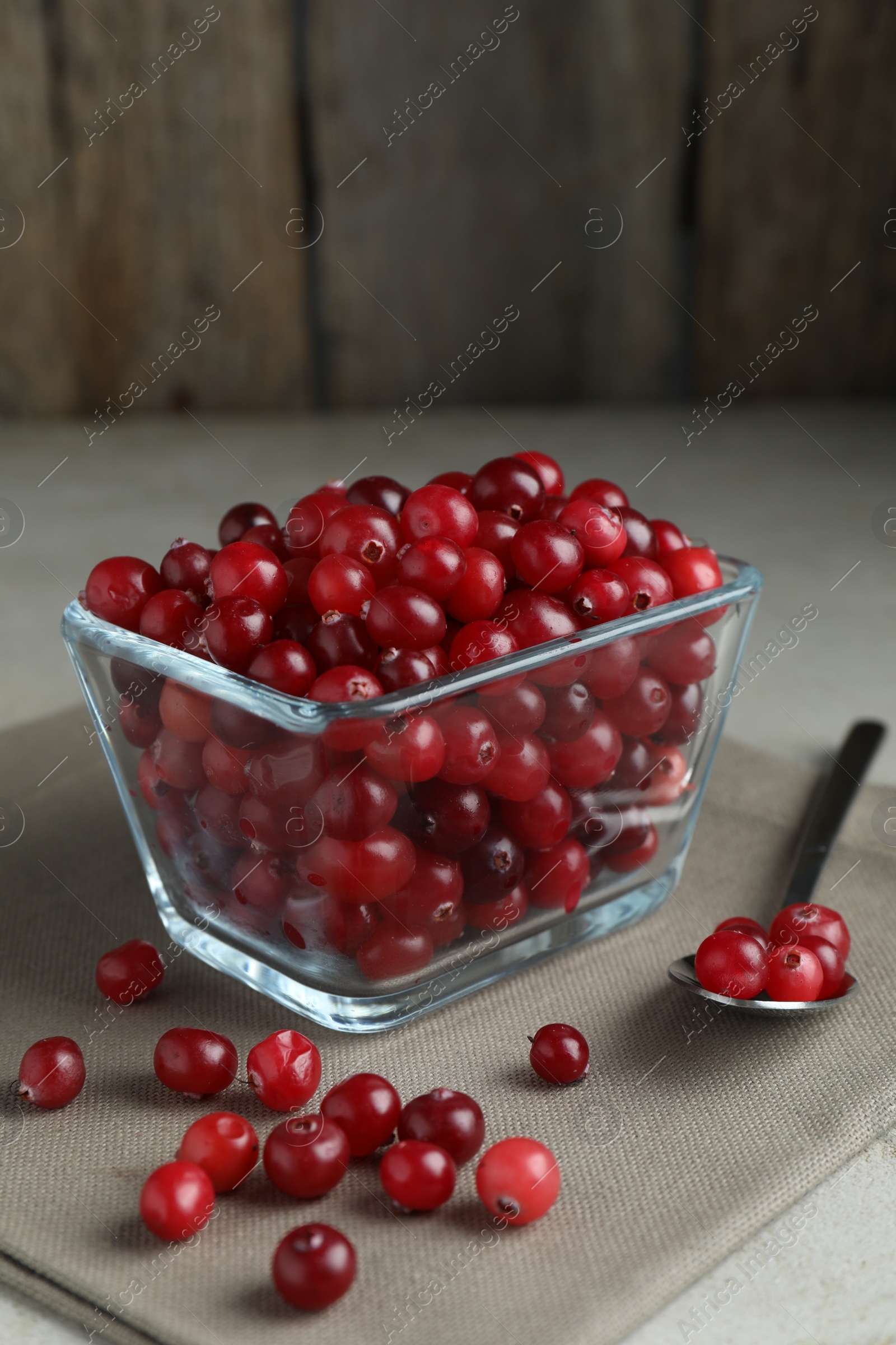 Photo of Cranberries in bowl and spoon on light grey table, closeup