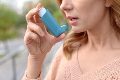 Photo of Woman using asthma inhaler outdoors, closeup. Health care