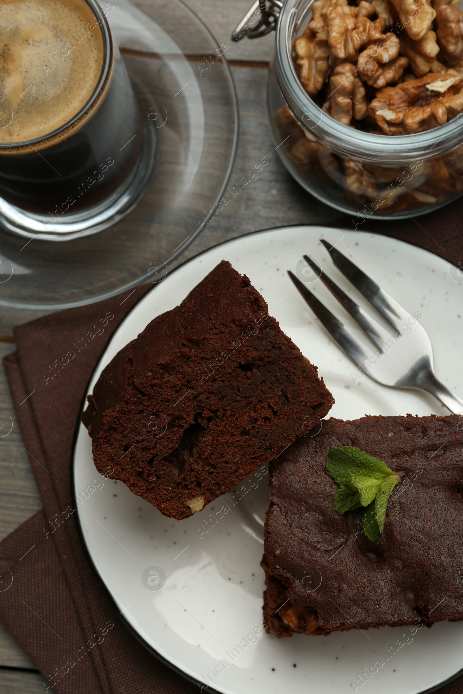 Photo of Delicious brownies served with walnuts and coffee on wooden table, flat lay