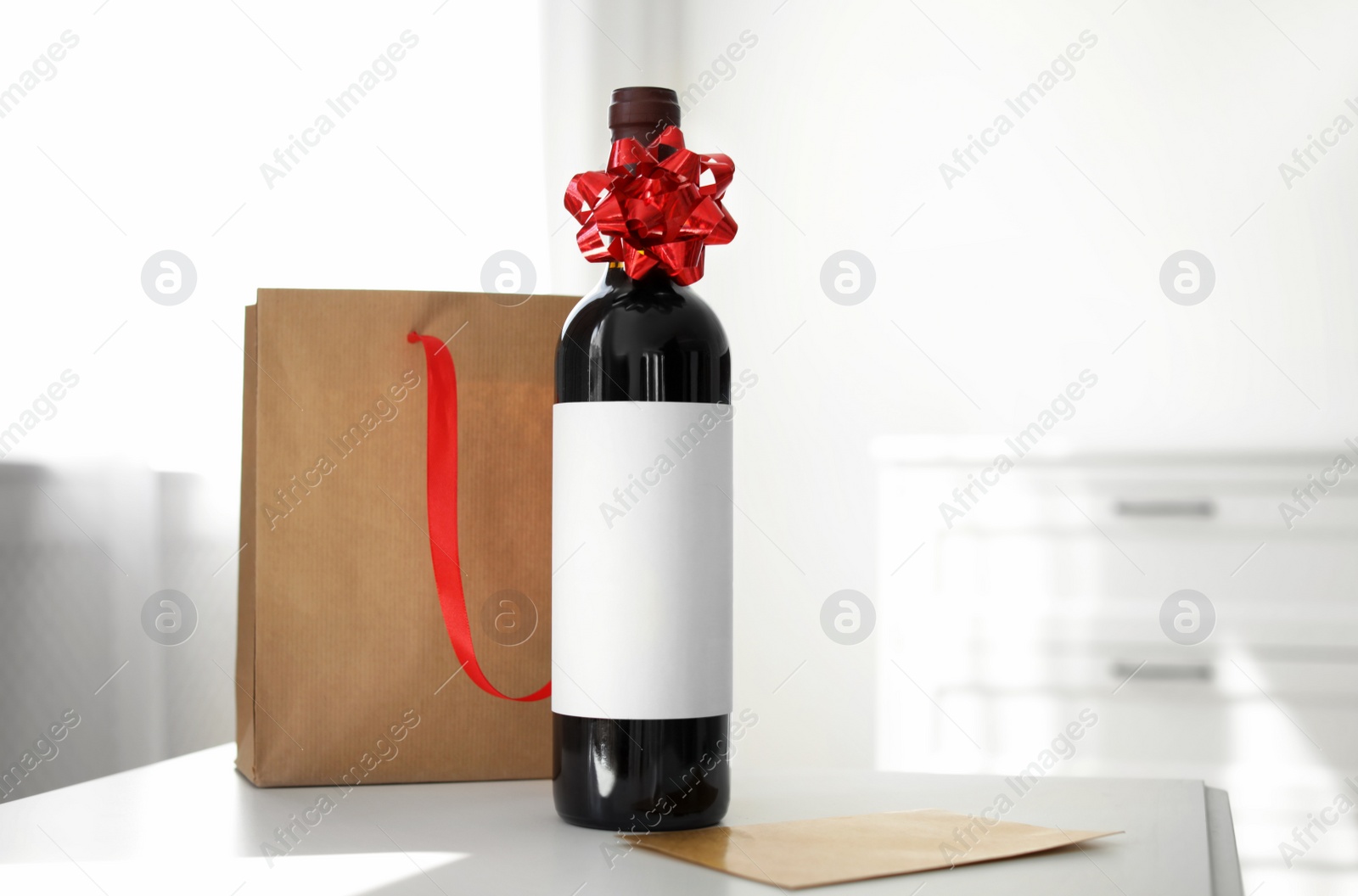 Photo of Bottle of wine, card and paper bag on table in light room. Space for text