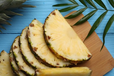 Photo of Slices of ripe juicy pineapple and green leaf on light blue wooden table, flat lay