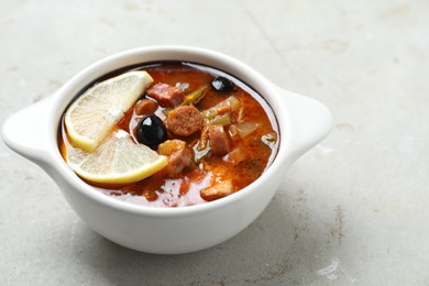 Photo of Meat solyanka soup with sausages, olives and vegetables in bowl on white textured table. Space for text