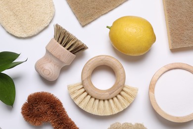 Photo of Cleaning brushes, lemon, baking soda, sponges and floral decor on white background, flat lay