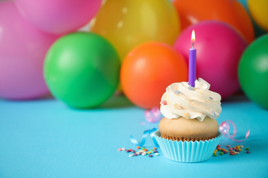 Birthday cupcake with candle and blurred balloons on background. Space for text