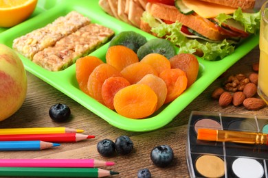 Serving tray of healthy food and stationery on wooden table, closeup. School lunch