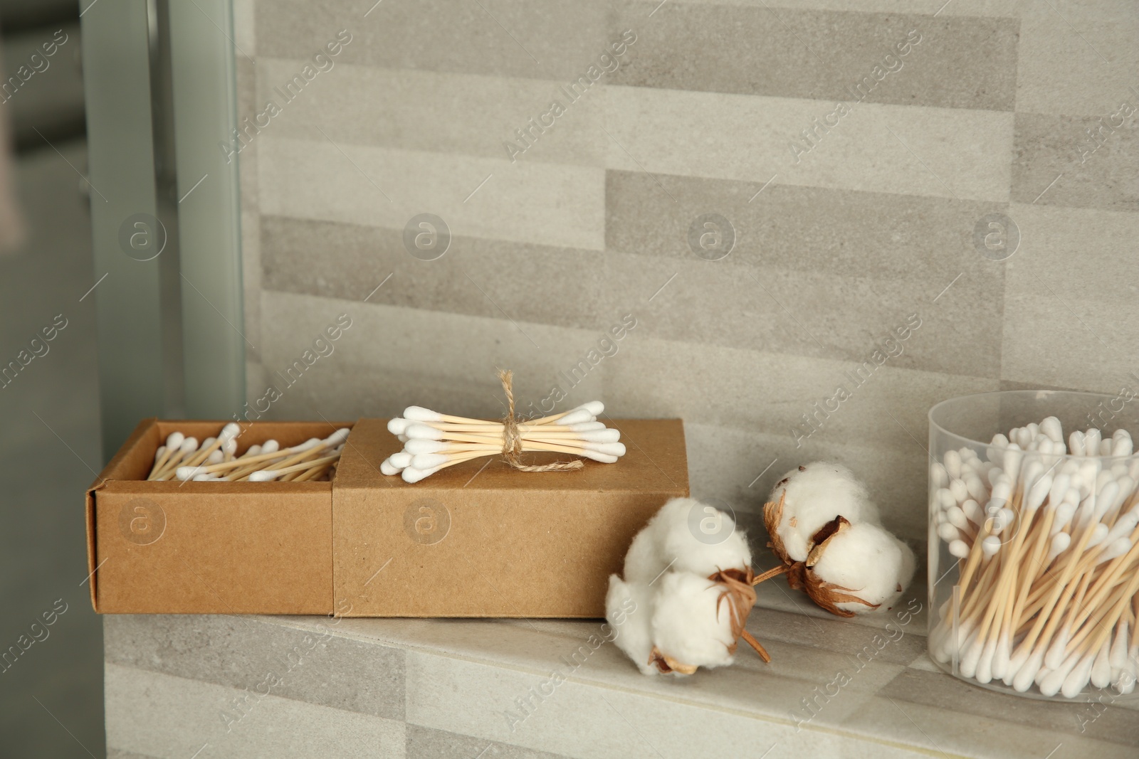 Photo of Cotton swabs and flowers on tiled surface in bathroom