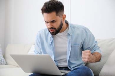Photo of Emotional young man with laptop at home. Online hate concept