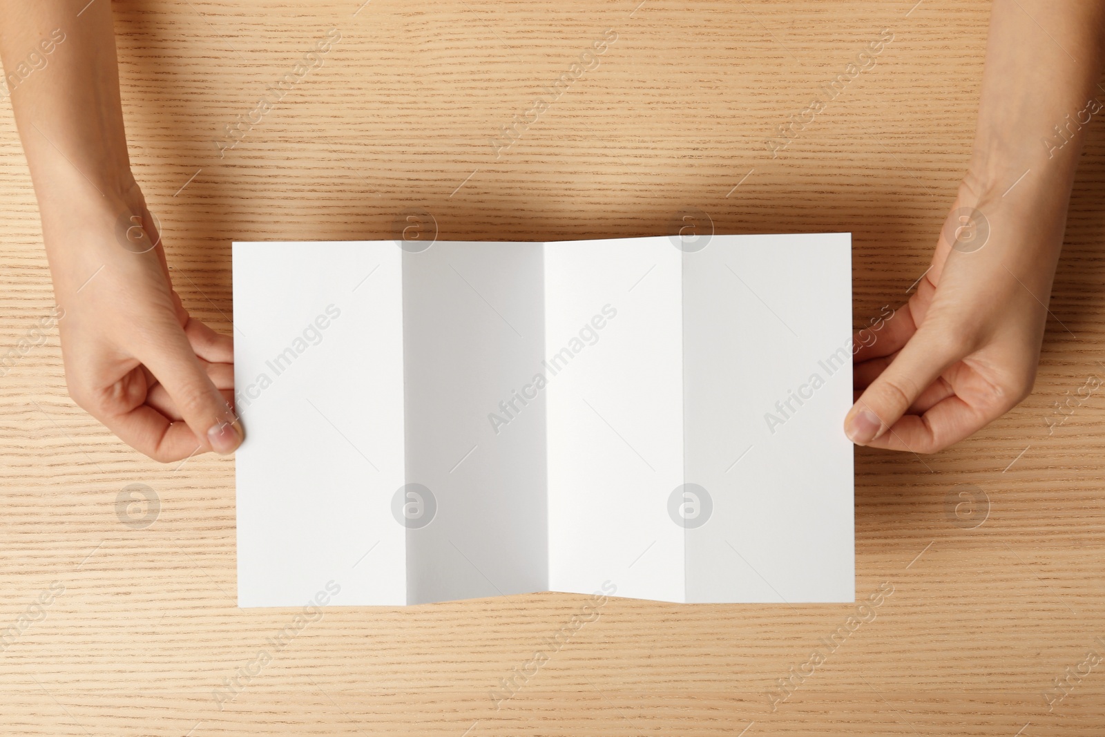 Photo of Woman holding blank brochure mock up on wooden table, top view