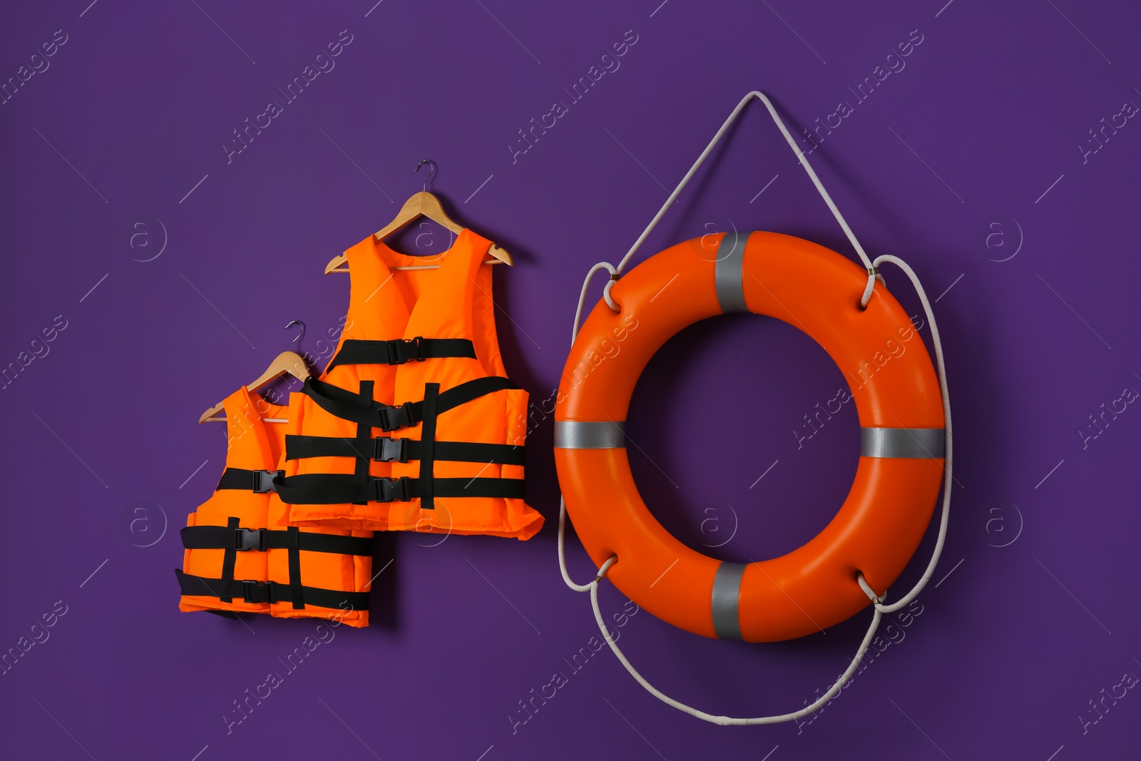 Photo of Orange life jackets and lifebuoy on violet background. Rescue equipment