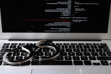 Photo of Handcuffs on modern laptop, closeup. Cyber crime