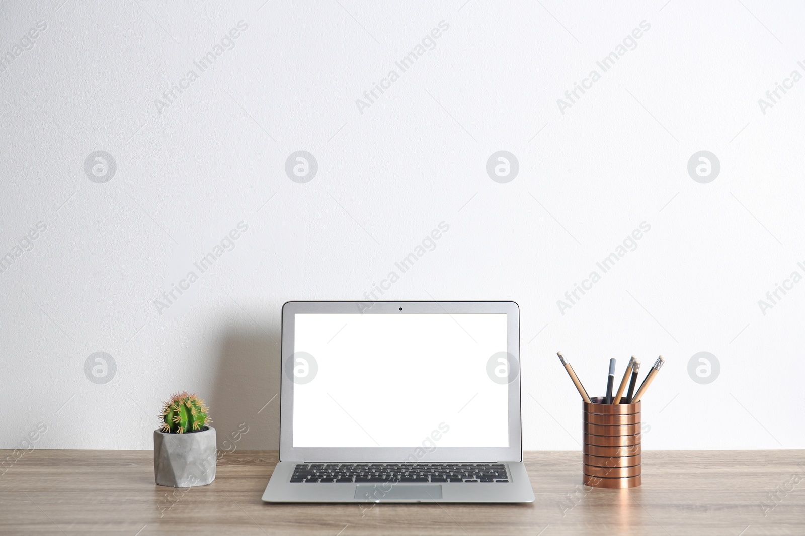 Photo of Modern computer monitor on table against white wall. Mock up with space for text