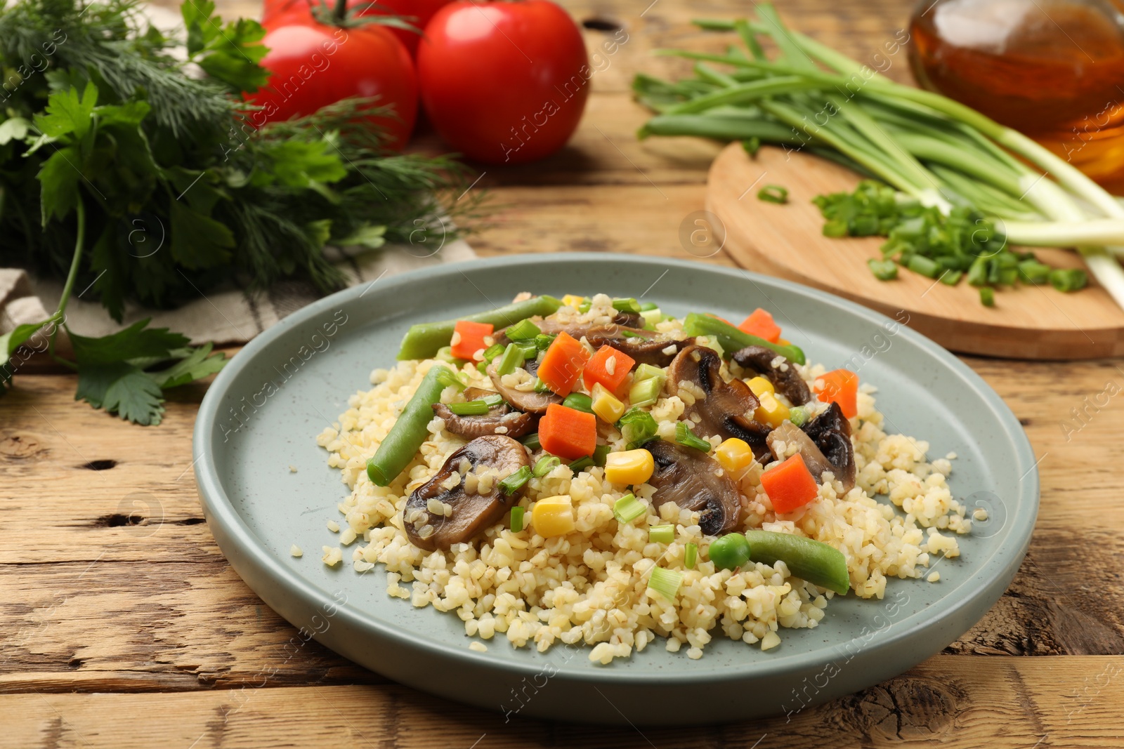 Photo of Delicious bulgur with vegetables and mushrooms on wooden table, closeup