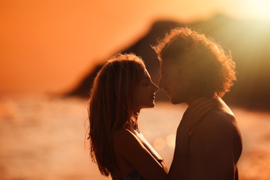 Photo of Young woman in bikini and her boyfriend on beach at sunset. Lovely couple